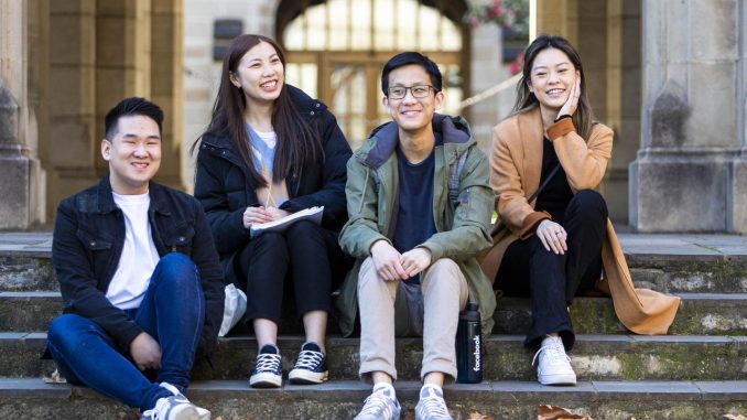 Chinese international students sit fornt the arch of taching building university