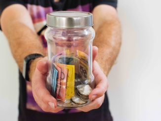 Photo shows A man holds a glass jar full of Australian dollar.