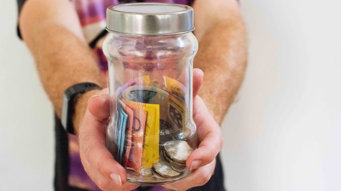 Photo shows A man holds a glass jar full of Australian dollar.