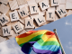 Mental health spelled out with wooden Scrabble tiles and a pride flag flying in the wind.