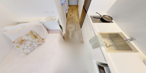 Screenshot of a UniLodge studio apartment at the University of Sydney, showing a bed positioned next to the kitchen sink and stovetop.